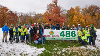 Group photo of event attendees in front of fall color trees holding a banner that reads 486 trees planted.
