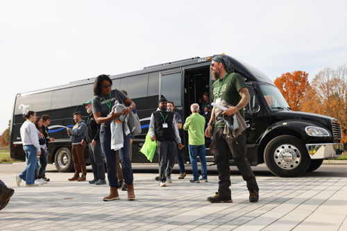 Students loading and unloading on a bus outside the front of the building