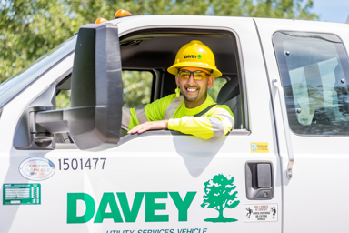 A man wearing PPE and a hardhat sitting in the driver's seat of a Davey Tree truck.