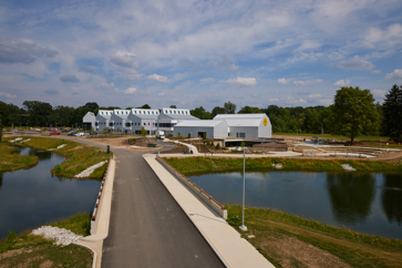A large, white facility on a campus with a pond, trees and plants.