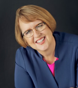 A headshot portrait of a woman with a blonde bob and glasses.