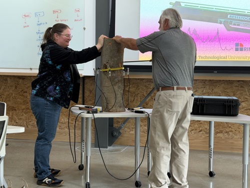 RJ Laverne and an employee touching a cut portion of a tree in front of the room to assess it for decay
