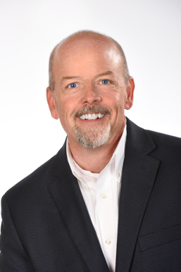 A professional headshot of a man with a black jacket and white dress shirt.