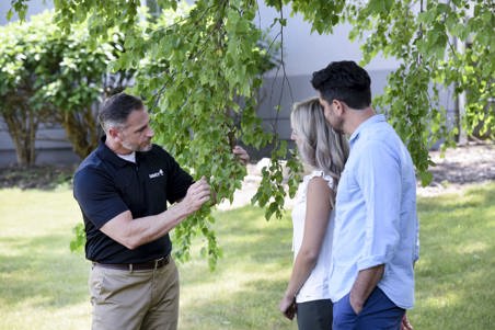 An arborist evaluating a tree with a young couple.