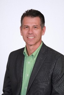 A headshot of a man with brown, short hair and a green dress shirt and gray jacket.