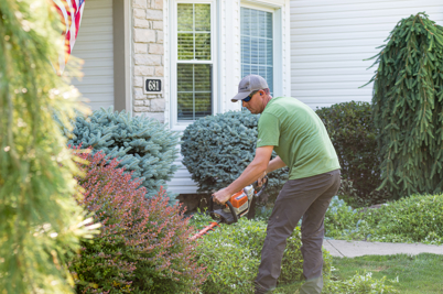 A man holding a landscaping tool and working in a front yard.