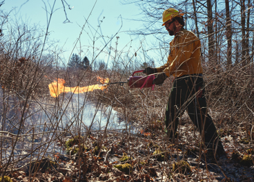 A man in a hard hat taming a small fire in dry grass